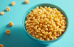 Bowl of golden puffed cereal on a bright blue background