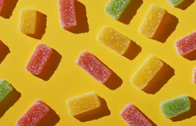 Sugar-coated red, yellow, and green sour gummy candies on yellow