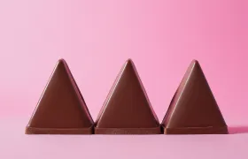 Three Toblerone chocolate triangles standing upright against a pink background