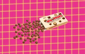 Whoppers box spilling malted milk balls on pink grid background