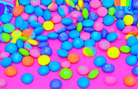 Colorful M&M’s candies scattered on bright pink background