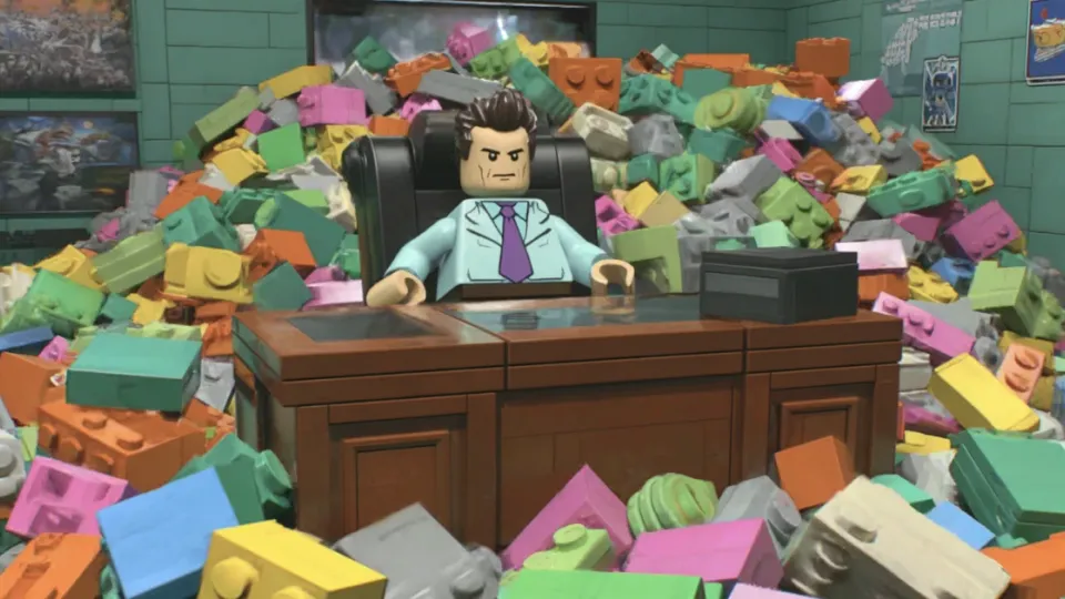 LEGO minifigure businessman at a desk buried in giant bricks